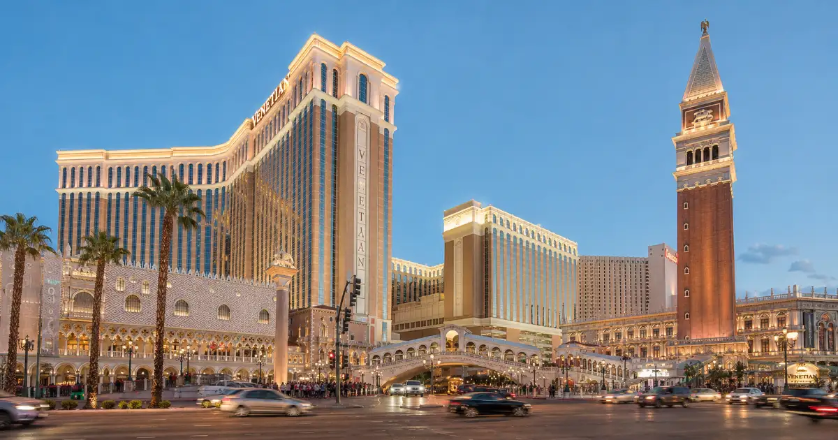 The Venetian Resort Las Vegas rises above its Italian-inspired Strip frontage, canal area, palm trees, and pedestrian walkways.