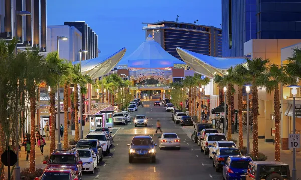 Evening view of Downtown Summerlin shopping district in Las Vegas featuring palm-lined pedestrian street, modern storefronts, parked cars, and illuminated canopy structure