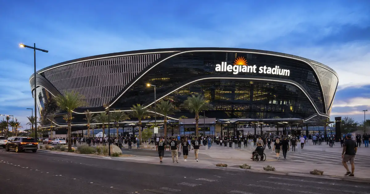 Guests approach the curved black-and-silver exterior and illuminated entrance of Allegiant Stadium near the Las Vegas Strip.