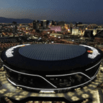 Allegiant Stadium in Las Vegas illuminated at night with Raiders logo and city lights in background
