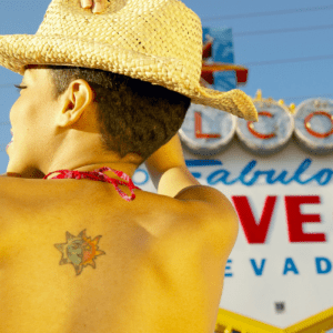 Cute girl with a tattoo on her back, wearing a straw hat, posing in front of the Welcome to fabulous Las Vegas Sign