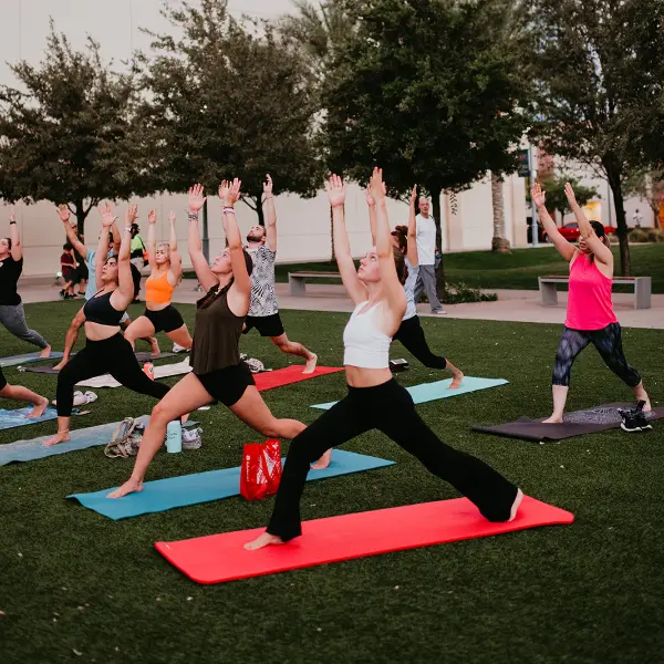 This is a picture of people doing yoga stretches at Fitness on the Lawn in Downtown Summerlin