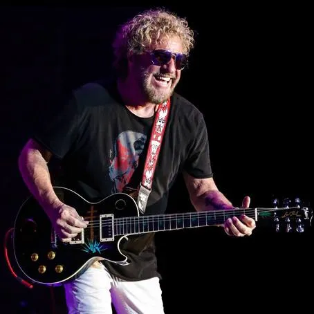rock guitarist with curly blond hair playing black les paul on stage in las vegas wearing sunglasses and graphic tee