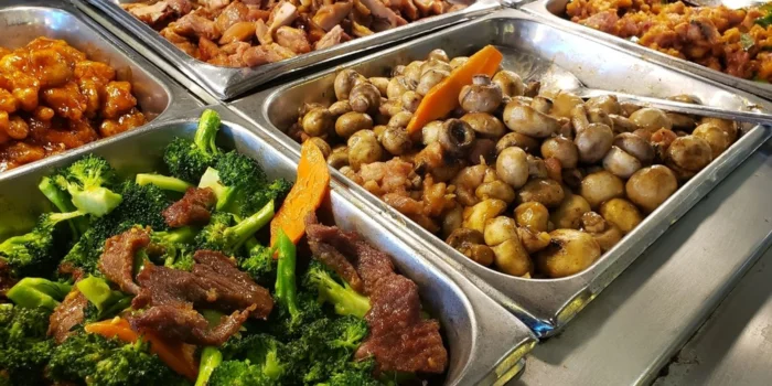 A close-up view of buffet trays filled with popular Chinese dishes like beef and broccoli and sautéed mushrooms at the Krazy Buffet, a value-focused Las Vegas restaurant located off the Strip.