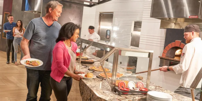 A chef working at a brick pizza oven at the Market Place Buffet inside the Rampart Casino, with happy diners serving themselves from the freshly prepared food line.