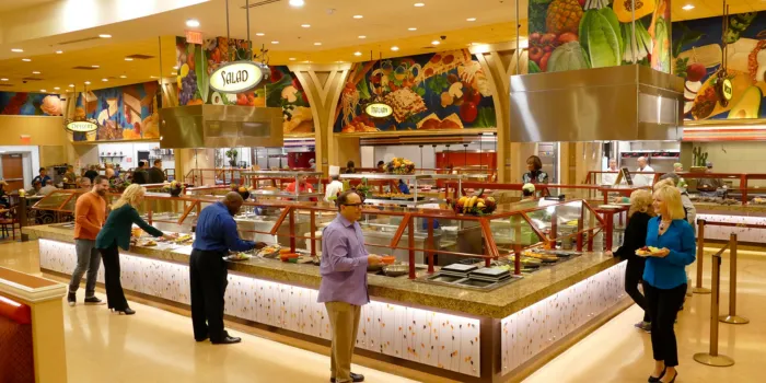 The brightly lit interior of the South Point Garden Buffet in Las Vegas, showing guests serving themselves from a variety of food stations with colorful murals and a casual atmosphere.