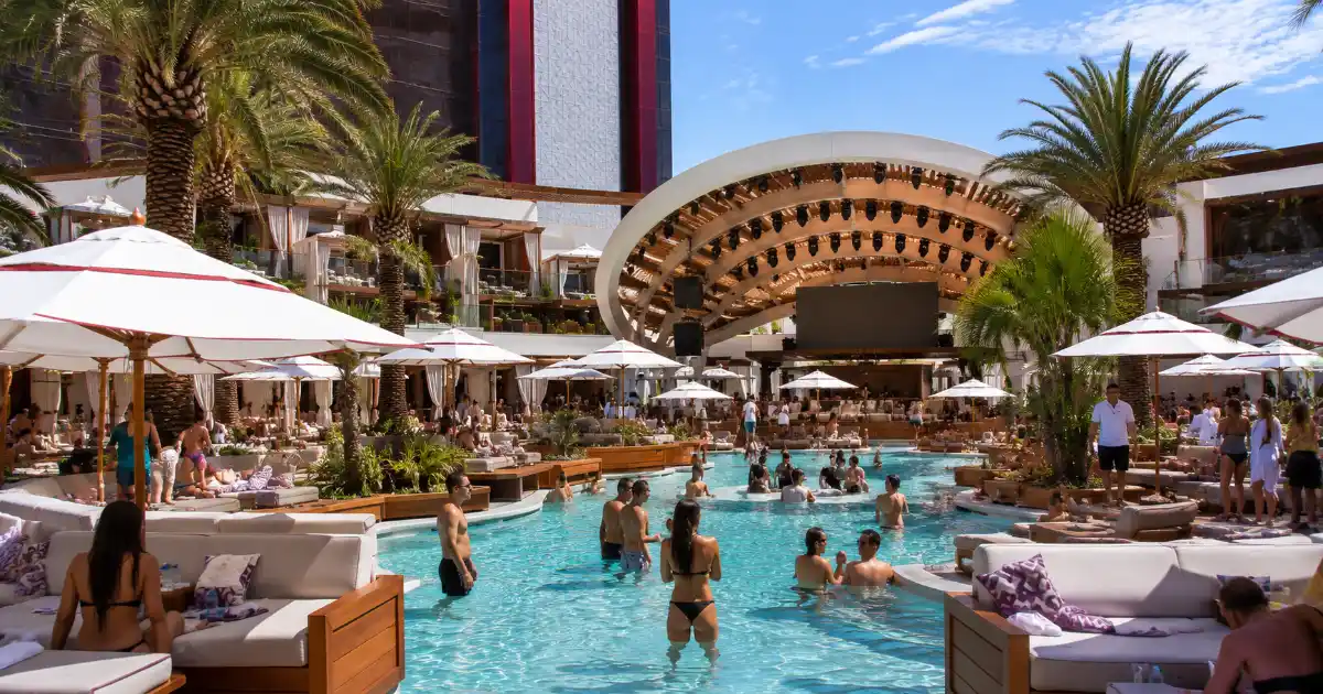 The main pool, curved stage canopy, palm trees, cabanas, and daybeds define AYU Dayclub at Resorts World Las Vegas.