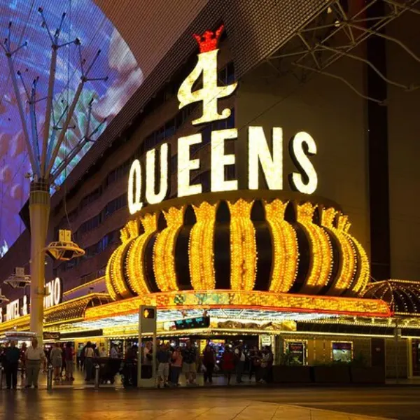 A dazzling night view of the Four Queens Hotel & Casino, located on Fremont Street in Las Vegas. The vibrant neon signage glows in bold reds and golds, illuminating the entrance with classic Vegas charm. Bright marquee lights flicker.
