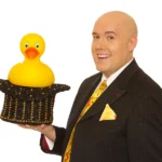 An image of Adam London from his Las Vegas show Laughternoon holding a plastic duck in a top hat
