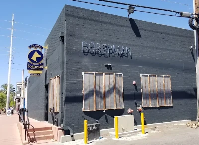 Exterior of The Doberman Drawing Room Cocktail Bar in the Las Vegas Arts District featuring dark gray building, metallic signage, dog logo, and urban street corner setting