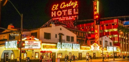 Nighttime view of the El Cortez Hotel & Casino in downtown Las Vegas, featuring glowing red and yellow neon signs for the hotel, coffee shop, and bar. The marquee advertises gambling and award-winning table games. Surrounding neon signs and vintage architecture evoke classic Vegas charm, making it a key stop on the Shadows of Sin City Ghost Tour.