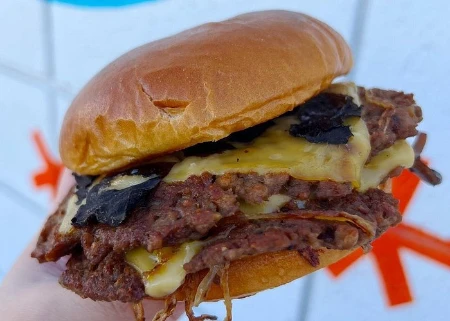 Handheld gourmet Vegan double cheeseburger from a Las Vegas Vegan food tour, stacked with two juicy plant-based patties, melted cheese, and black truffle slices on a toasted bun.