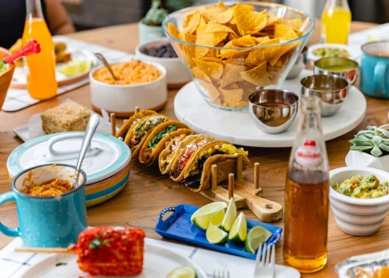 Colorful vegan Mexican food spread from a Las Vegas food tour, featuring assorted tacos with plant-based fillings, elote street corn, guacamole, tortilla chips with salsa, and Jarritos soda on a rustic wooden table.