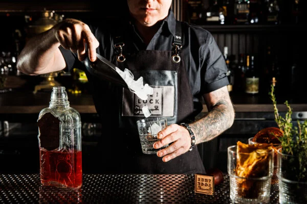 Image for the Cabinet of Curiosities Mixology Masterclass, showing a bartender preparing a cocktail on a curated bar counter.