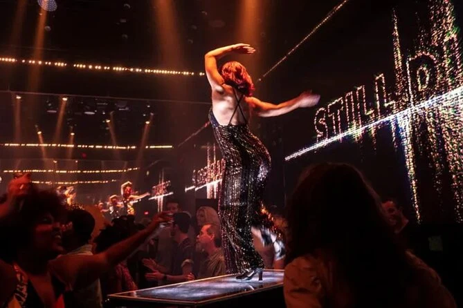 Performer in sequined outfit strikes dramatic pose on raised platform during DiscoShow at The LINQ in Las Vegas, surrounded by vibrant lighting and an engaged nightclub crowd.