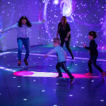 Children and adults playing in a motion-responsive light room at Electric Playhouse Las Vegas, surrounded by vibrant digital visuals and immersive patterns