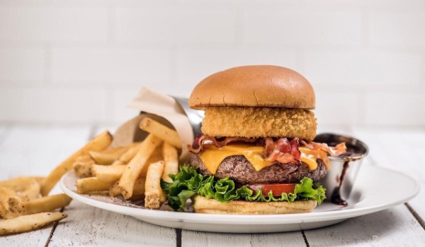 Hard Rock Cafe Las Vegas bacon cheeseburger served with crispy fries, barbecue dipping sauce, and a fried onion ring on a toasted bun.