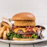 Gourmet bacon cheeseburger with onion ring served with golden fries and dipping sauce at Hard Rock Cafe Las Vegas on white tile background