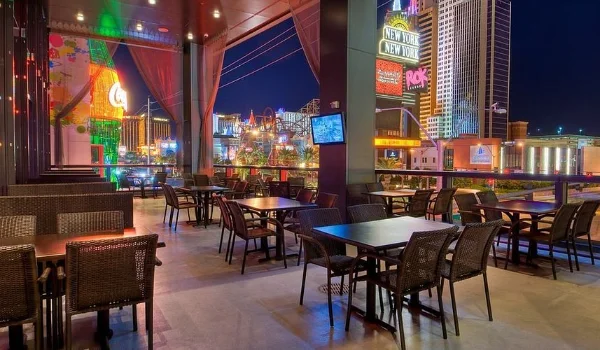 Second-floor outdoor dining area at Hard Rock Cafe Las Vegas with wicker chairs, neon-lit Strip views, and red curtains framing the vibrant city nightlife.
