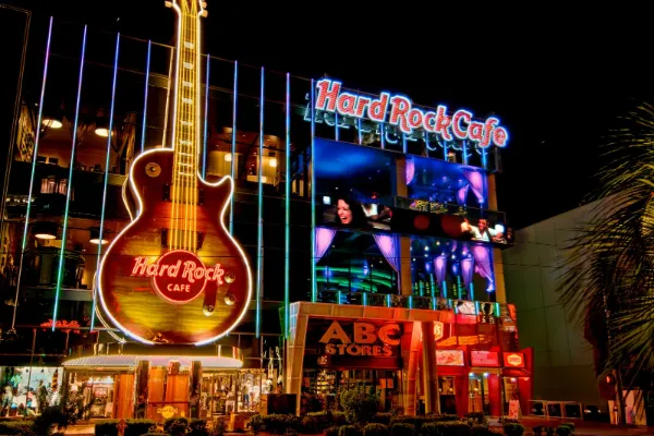 Exterior of Hard Rock Cafe Las Vegas at night featuring a giant illuminated guitar sign, neon lights, and palm trees along the Strip.