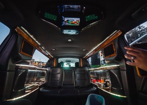 Interior of a luxury limousine in Las Vegas featuring black leather seats, ambient ceiling lighting, digital displays, and upscale wood trim accents