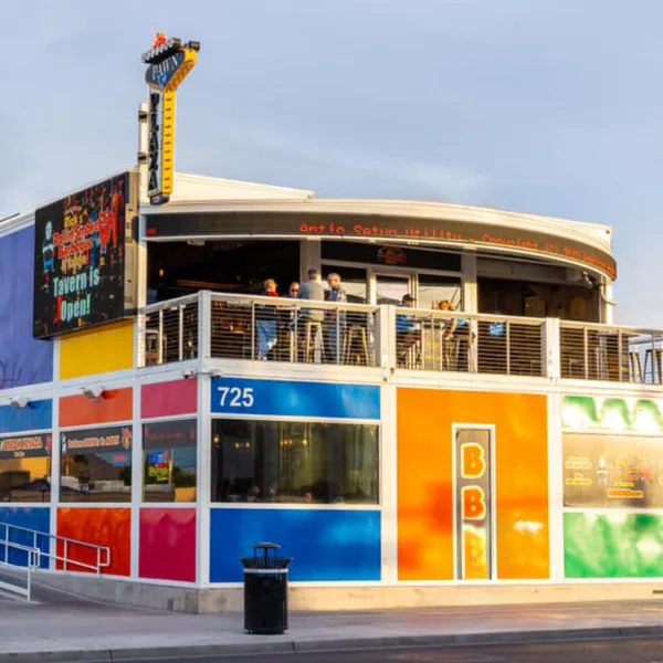 Colorful two-story building at Pawn Plaza Las Vegas featuring bright red, blue, yellow, and orange exterior walls, open-air tavern seating, and vertical Pawn sign with digital marquee