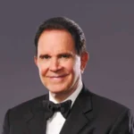 Formal portrait of Rich Little wearing black tuxedo and bow tie against plain background, representing his legacy as a comedy impersonator in Las Vegas