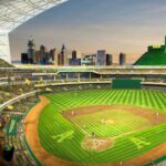 Professional baseball game in urban stadium at sunset with city skyline and multi-tiered seating