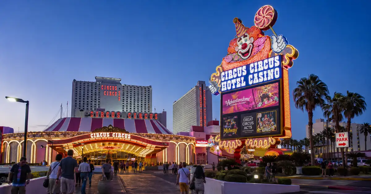 Circus Circus Hotel & Casino features its colorful clown marquee, permanent resort signage, hotel towers, palm trees, and north-Strip entrance.