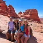 Family hiking at Arches National Park in Utah sitting on red rock formation with layered sandstone and clear blue sky