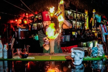 Bartender at The Golden Tiki in Las Vegas Chinatown performing a flaming cocktail presentation with dramatic fire colorful lighting and skull themed bar decor