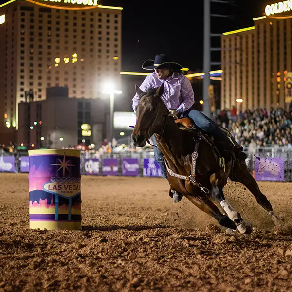 Barrel racer at Helldorado Days Fall Rodeo in Las Vegas maneuvering horse around colorful Las Vegas barrel under city lights