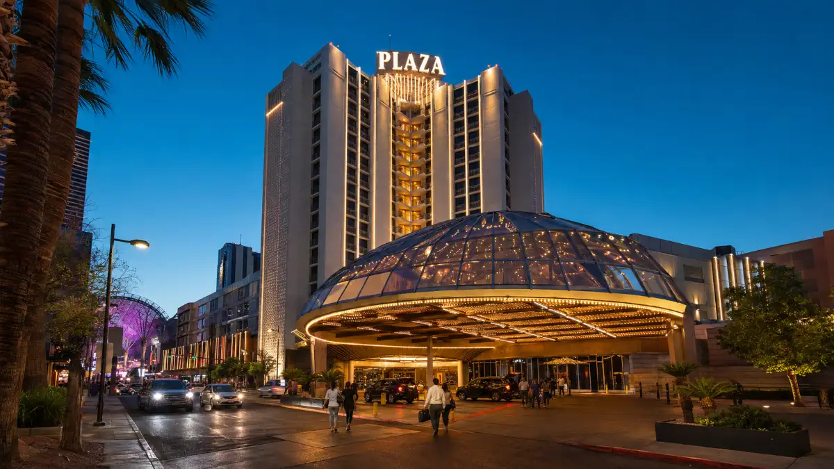 Guests arrive beneath the illuminated Main Street canopy of Plaza Hotel & Casino in downtown Las Vegas at blue hour.