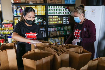 volunteers packing food bags at salvation army henderson corps pantry in las vegas with shelves of canned goods and boxed meals