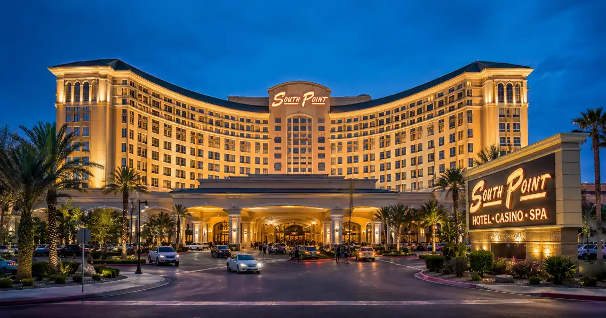 The illuminated hotel tower, palm trees, landscaped entrance, and permanent signage of South Point Hotel, Casino & Spa in Las Vegas.