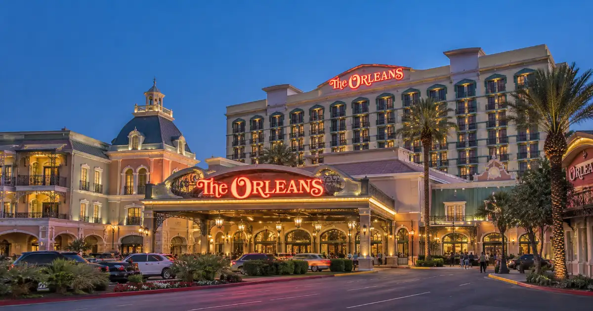 The illuminated New Orleans-inspired façade, hotel tower, palm trees, and main entrance of The Orleans Hotel & Casino in Las Vegas.