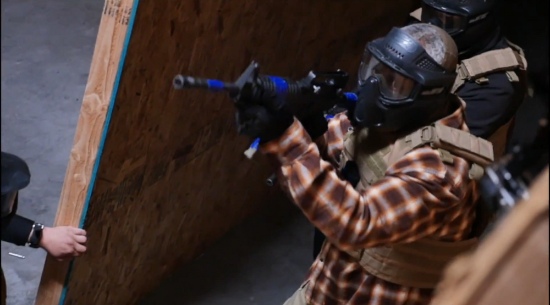 Man in tactical gear participating in indoor training simulation with non-lethal rifles near wooden wall structure in Las Vegas