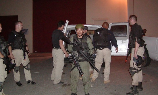 Armed personnel in tactical gear conducting nighttime training near white vehicle with red wall and artificial lighting in Las Vegas