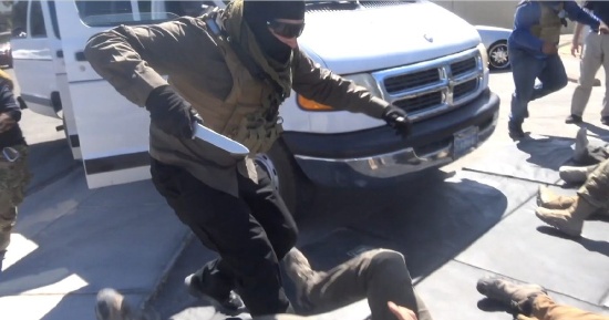 Outdoor tactical training simulation in Las Vegas showing individuals in military gear practicing knife defense and close-quarters combat near white van