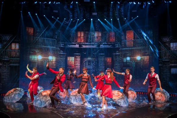 cast of wow the vegas spectacular performing on water-covered stage at rio hotel in las vegas with dancers in red costumes and dramatic urban backdrop