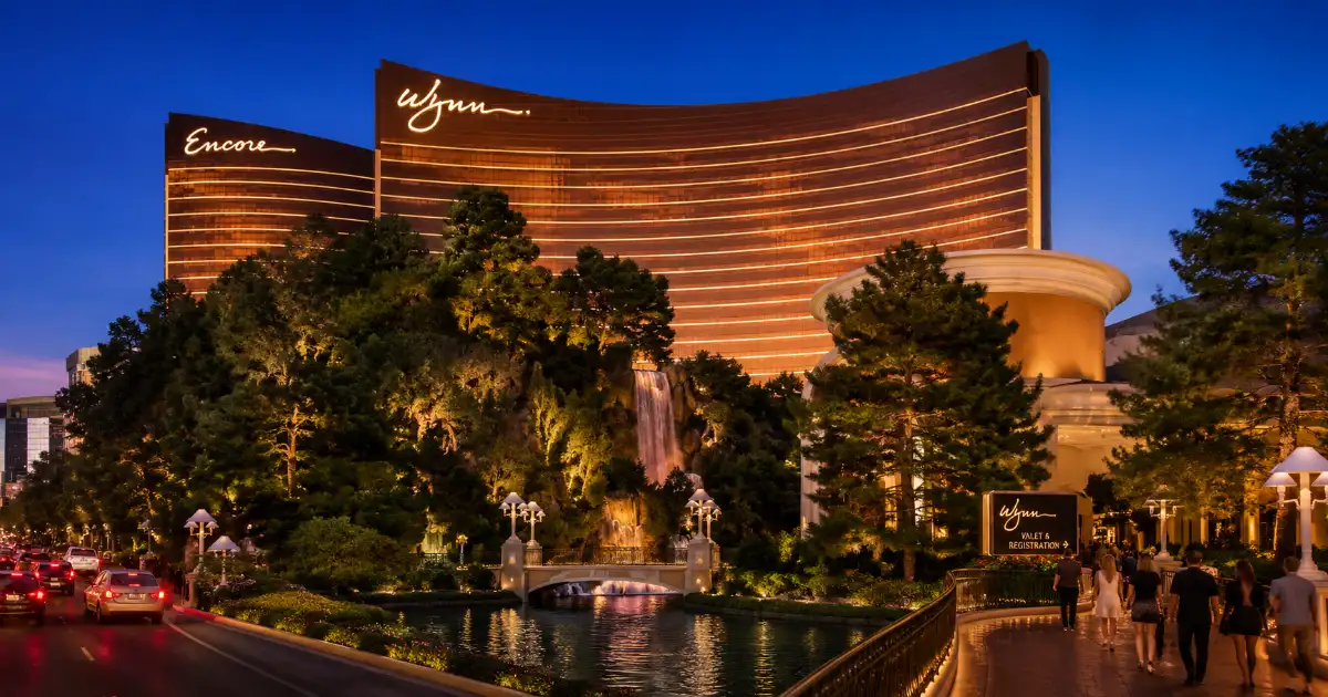 The curved bronze-glass tower, permanent rooftop sign, waterfall, and landscaped entrance identify Wynn Las Vegas on the Strip.