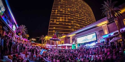 A massive crowd partying around the pool at Encore Beach Club at Night with the lit up cabanas and Las Vegas Strip in the background