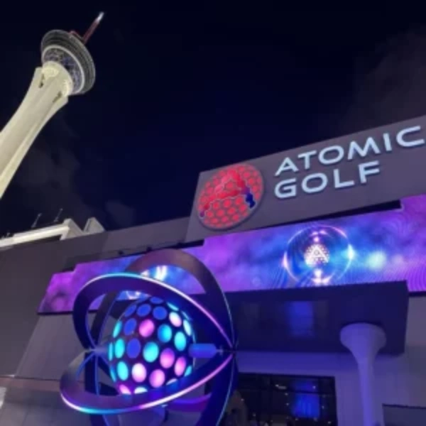 illuminated exterior of atomic golf venue in las vegas with glowing atomic sculpture and signage near the strat hotel