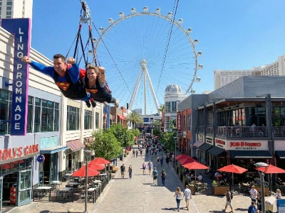 People flying on the Fly LINQ Zipline over the LINQ Promenade at night.