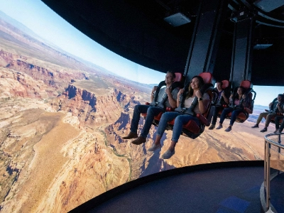 A group of people sitting in motion seats facing a large dome screen at the FlyOver attraction.