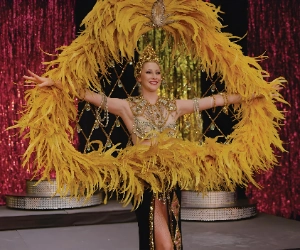 performer in gold and black costume with yellow feather fan on stage at grant philipo showgirl museum in las vegas