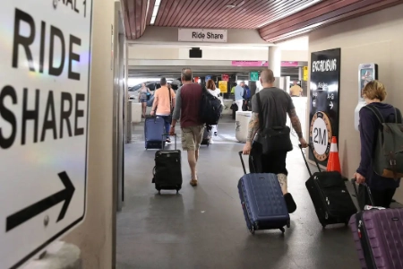 travelers walking through las vegas airport terminal toward designated ride share pickup area with directional signage and luggage