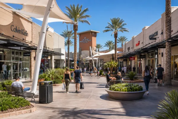 Shoppers walk between outlet storefronts, palm trees, seating areas, and shade canopies at Las Vegas North Premium Outlets.