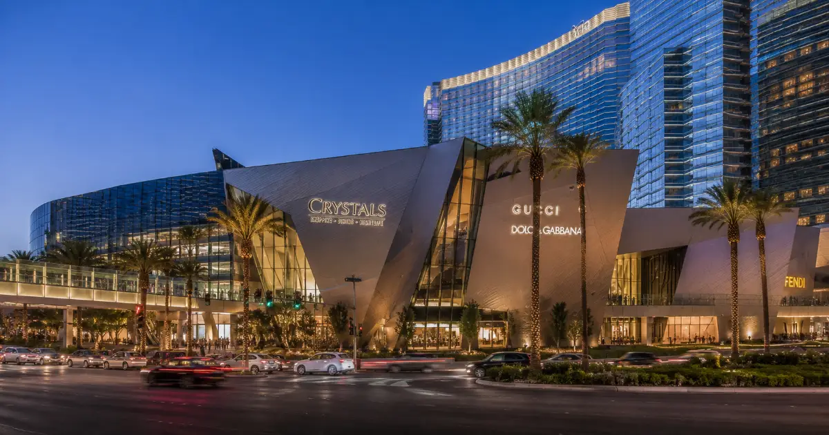 The angular metal-and-glass exterior, palm trees, and luxury storefronts of The Shops at Crystals on the Las Vegas Strip.