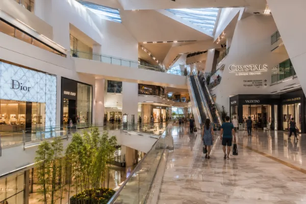 Visitors walk through the bright multilevel atrium, angular architecture, escalators, and luxury storefronts inside The Shops at Crystals.